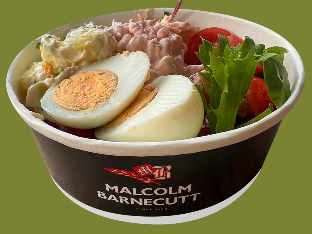 Front view of blue salad bowl with Malcom Barnecutt logo. Filled with halved boiled egg, potato salad, coleslaw, tomatoes, and salad leaves.