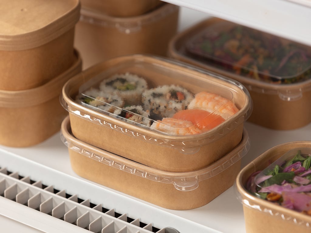 Close up of stacked PE Stagione trays with clear lids in chiller, filled with sushi and sushi rolls.