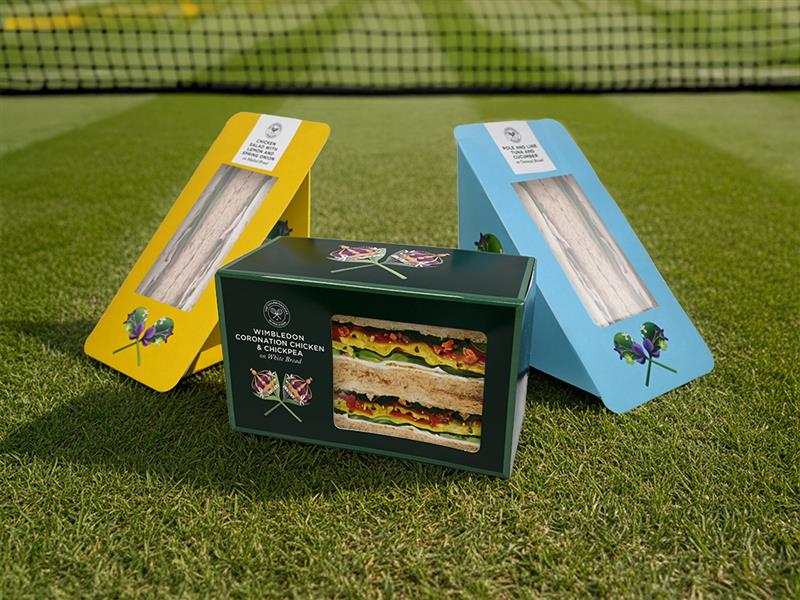 Two wedge sandwich packs in yellow and blue, and one square sandwich pack in green, on turfed pitch surface with net in background.