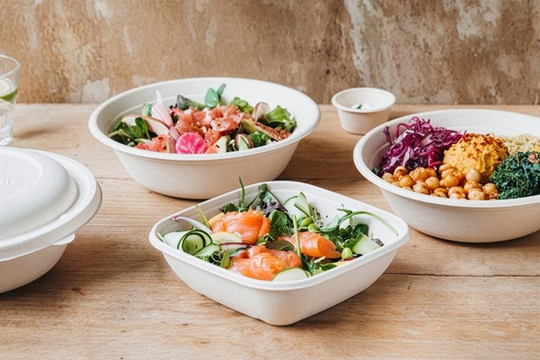 Three pulp takeaway containers filled with a selection of salads, all on a wooden table. Pulp pack with lid, small pulp pot, and glass of water in background.